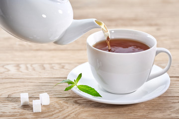 Cup with tea and teapot on wooden background
