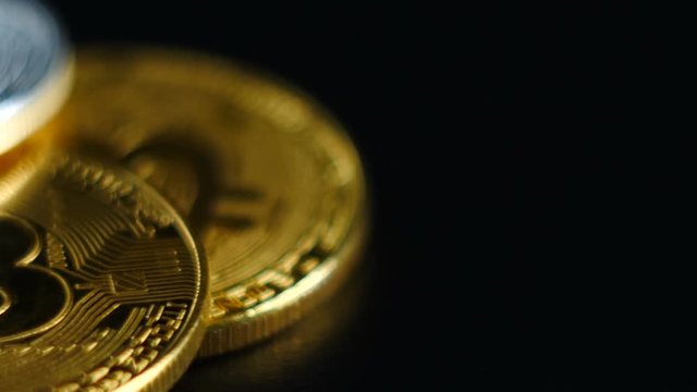 Gold and silver bitcoins lie on a black background. Camera dolly.