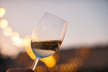 Hand with a glass of white wine checking wine quality at sunset light - 175055401
