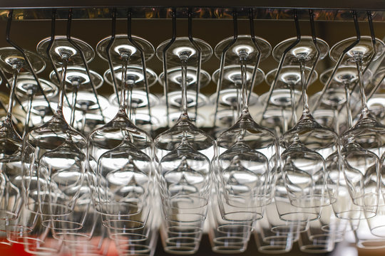Image of wine glasses stacked on black metal hanging bar glass racks in a bar, nightclub or a restaurant with light shining through them.