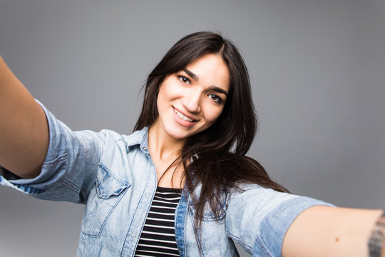 Happy young cute woman making selfie over gray background.