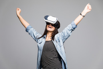 Attractive and happy woman using virtual reality goggles celebrate victory gesture on grey background. VR headset.