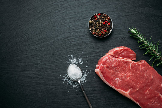 Raw beef steak on black slate background
