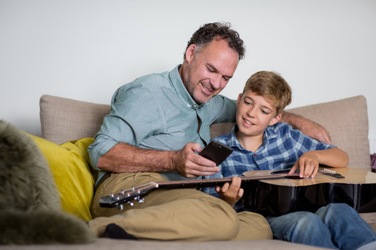 Father teaching son how to play guitar using a smartphone