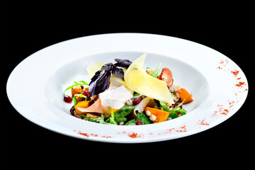 Tasty, delicious salad with baked pumpkin in a white plate isolated on black background. Autumn menu in an Italian restaurant