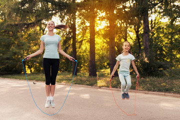 Girl and her mother jumping rope on the path in the park