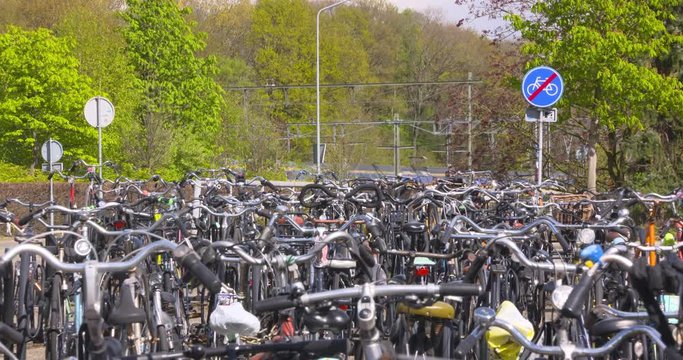 Unguarded bicycle parking facility at railway station + traffic sign indicating end of cycle path. Arriving commuter train NS (Dutch Railways) in background. EDE, THE NETHERLANDS - APRIL 2017