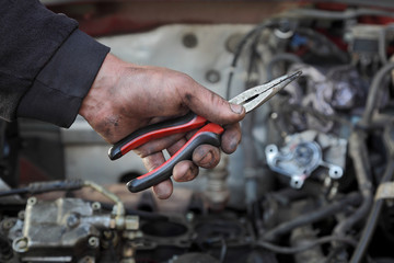 Dirty mechanic hand  hold long nose pliers in hand with car engine in background