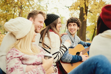      Friends having a good time in park at autumn/ singing and playing guitar 