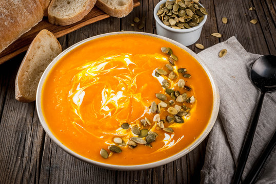 Traditional fall and winter dishes, hot and spicy pumpkin  soup with pumpkin seeds, cream and freshly baked baguette, on old rustic wooden table, copy space