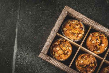 Autumn and winter baked pastries. Healthy pumpkin muffins with traditional fall spices, pumpkin seeds. In old wooden box, Black stone table, copy space top view