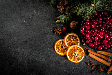 Ingredients for Christmas, winter baking cookies. Gingerbread, fruitcake, seasonal drinks. Cranberries, dried oranges, cinnamon, spices on a black stone table, copy space top view