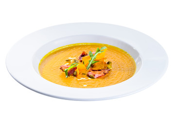 Delicious and appetizing pumpkin cream soup with chips in a white plate isolated on black background. Autumn menu in an Italian restaurant. Photo for menu design