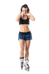 Relaxed joyful fit woman in roller inline skates holding headphones enjoying music. Full body...