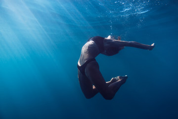 Fototapeta na wymiar Slim woman swimming in underwater. Sun rays in underwater