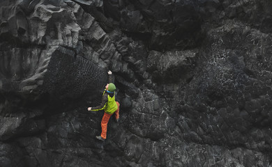 male rock climber. rock climber climbs on a black rocky wall on the ocean bank in Iceland, Kirkjufjara beach. man makes hard move without rope.