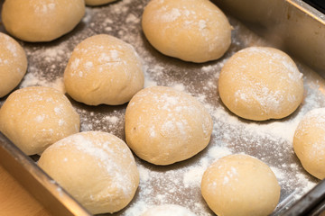 Fototapeta na wymiar Authentic home kitchen, freshly made white bread rolls proving sprinkled with with flour ready for baking on tray