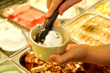 Female hand with scoop takes ice cream from the fridge and serving in ceramic white cups. Woman taking scoop of tasty ice cream. Fridge with ice cream. Woman works in ice cream shop. Pastry shop.