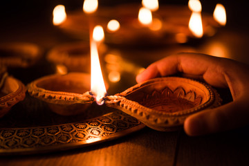 Happy diwali - Hand holding or lighting or arranging diwali diya or clay lamp in brass plate, selective focus