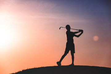 Fototapeta na wymiar silhouette of boy golfer with golf club at sunset