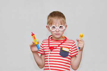 Cute boy playing doctor. Toy syringe, glasses and phonendoscope. Portrait