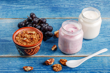 Healthy breakfast ingredients.Homemade yogurt in glass jars, ceramic bowl with oat flakes, walnuts, grapes on light blue background, copy space