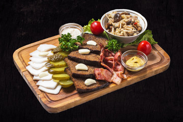 Snack with bacon, fried bread, fat, marinated mushrooms and cucumbers on a dark wooden background