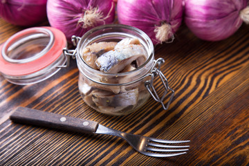 Herring with onion in a jar on a wooden table