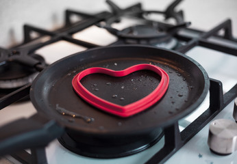 A man cooks an omelette in a beautiful kitchen on a gas cooktop in a heart shaped form. Conceptual...