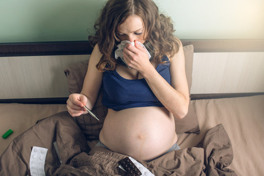 Pregnant woman in bed with pills and a thermometer. Sick with the flu or a cold.