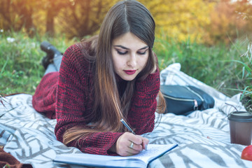 Beautiful woman writer writing with pen autumn story in her notebook. Concept of education and working with nature
