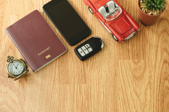 top view. travel object include retro clock, passport, key, car, plant in vase and smart phone placed on wooden background. image for toy, hobby, business concept