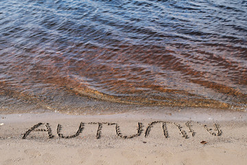 Word autumn written on sand background