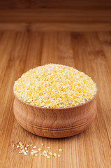 Corn grits in wooden bowl on brown bamboo board, closeup. Rustic style, healthy dietary groats  background.