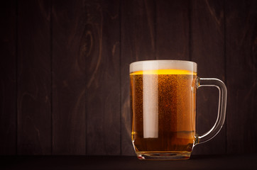 Mug beer glass with golden sparkling lager on dark wood board, copy space. Template for advertising, design, branding identity, restaurant menu, cover.