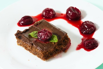 Square pieces of homemade brownie served on white plate with cherries and mint leafs