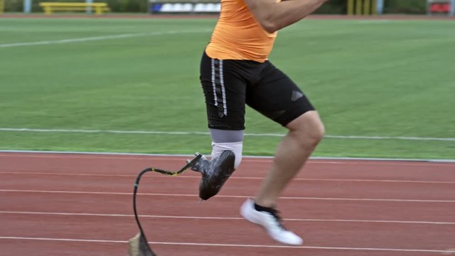 Tilt down side view of amputee athlete with prosthetic limb running on stadium track while exercising outdoors