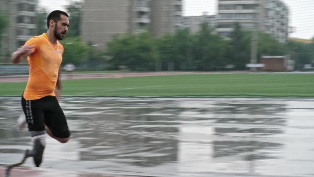 Tilt up of professional blade runner training on stadium track at rainy day