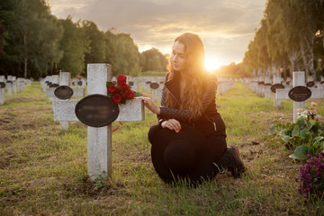 Sad woman in the cemetery, holding a bouquet of roses in her hand