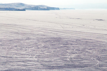 Car trails on the frozen lake surface covered with snow/ Lake Baikal