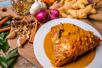 Delicious fish head curry served in a white plate over a wooden cutting board with some spices