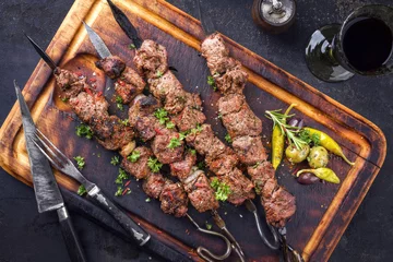 Foto auf Leinwand Traditional Russian shashlik on a barbecue skewer and red wine as top view on an old burnt cutting board © HLPhoto
