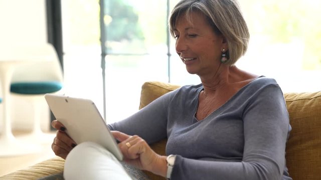 Mature woman in sofa connected with digital tablet