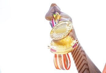 Blurred of hands raised and holding two gold medals with Thai ribbon against blue sky background to show team success in business, Winners success award concept.