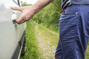 The man opens the door of the car with his hand, which stands on the forest road. Close-up.
