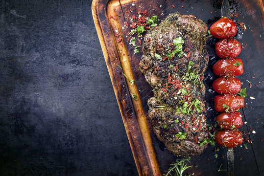 Barbecue lamb roast with skewered tomatoes as close-up on an old burnt cutting board