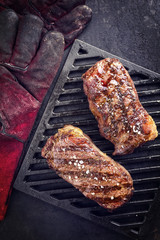 Two barbecue dry aged Kobe roast beef as close-up on a grillage with gloves