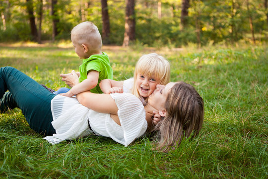 Family concept, mother playing with her kids and kissing her daughter on the grass