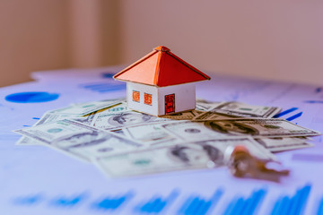 Business Real Estate Concept, House model with a key and dollar bills put on paper graph on wooden background.