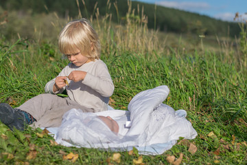 A blond boy with younger newborn brother siiting on a grass during outing